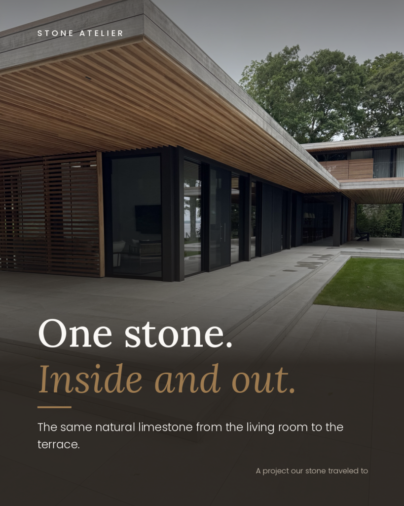 One Stone Inside and Out: Using the Same Natural Stone for Interior Floors and Outdoor Living 1 Large-format grey natural stone terrace with matching step treads and risers under a wood slat overhang beside a lawn.